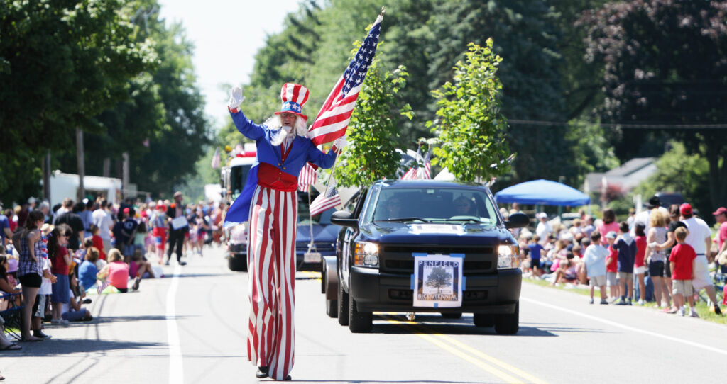 Penfield, New York, USA - July, 3 2010: A man on stilts dressed as Uncle Sam carries a large US flag and waves to the crowd during the Penfield town Independence Day parade.