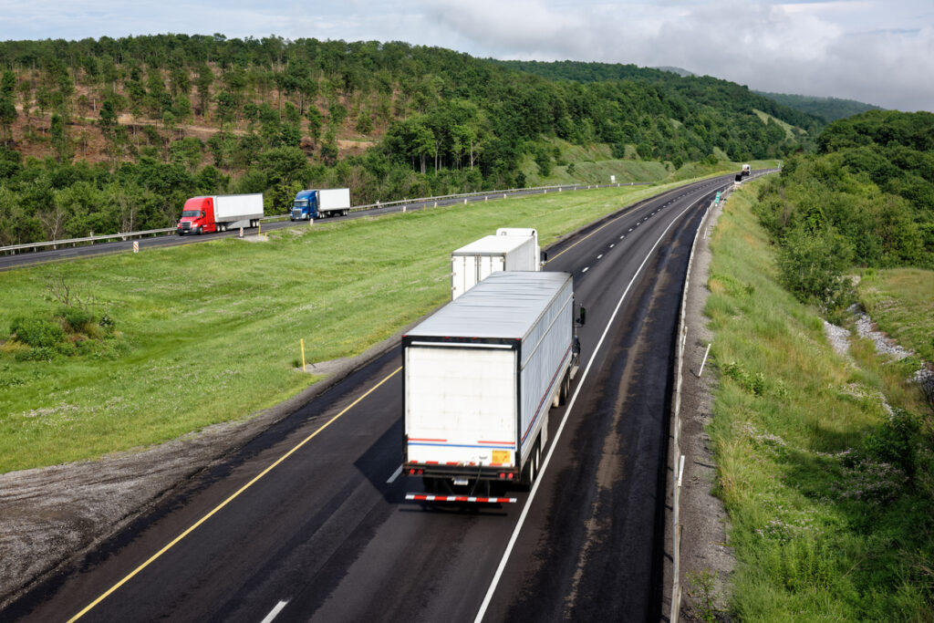 Trucks moving down an interstate highway through the scenic eastern mountains, tractor trailers in transportation and trucking industry hauling freight.