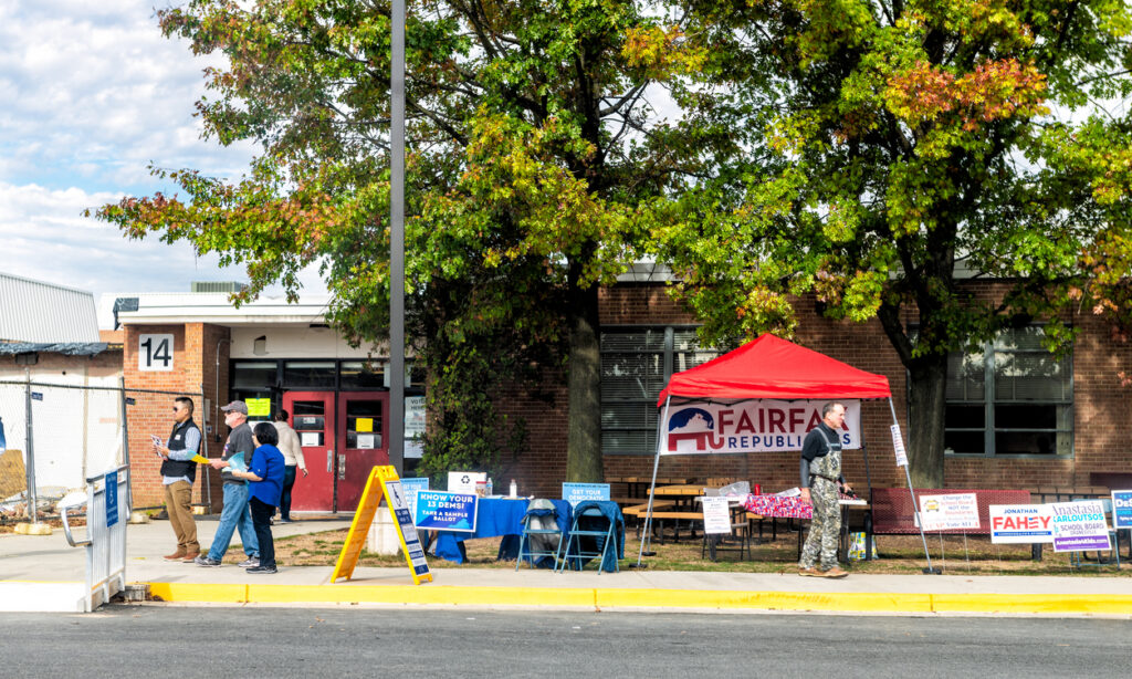 Herndon, Virginia - November 5, 2019: High school polling station with sidewalk road and Fairfax Republicans booth with people handing out sample ballots and flyers