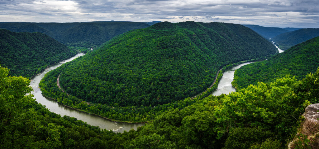 Panoramic view of the New River Gorge in West Virginia with lush green mountains and a winding river under a cloudy sky.